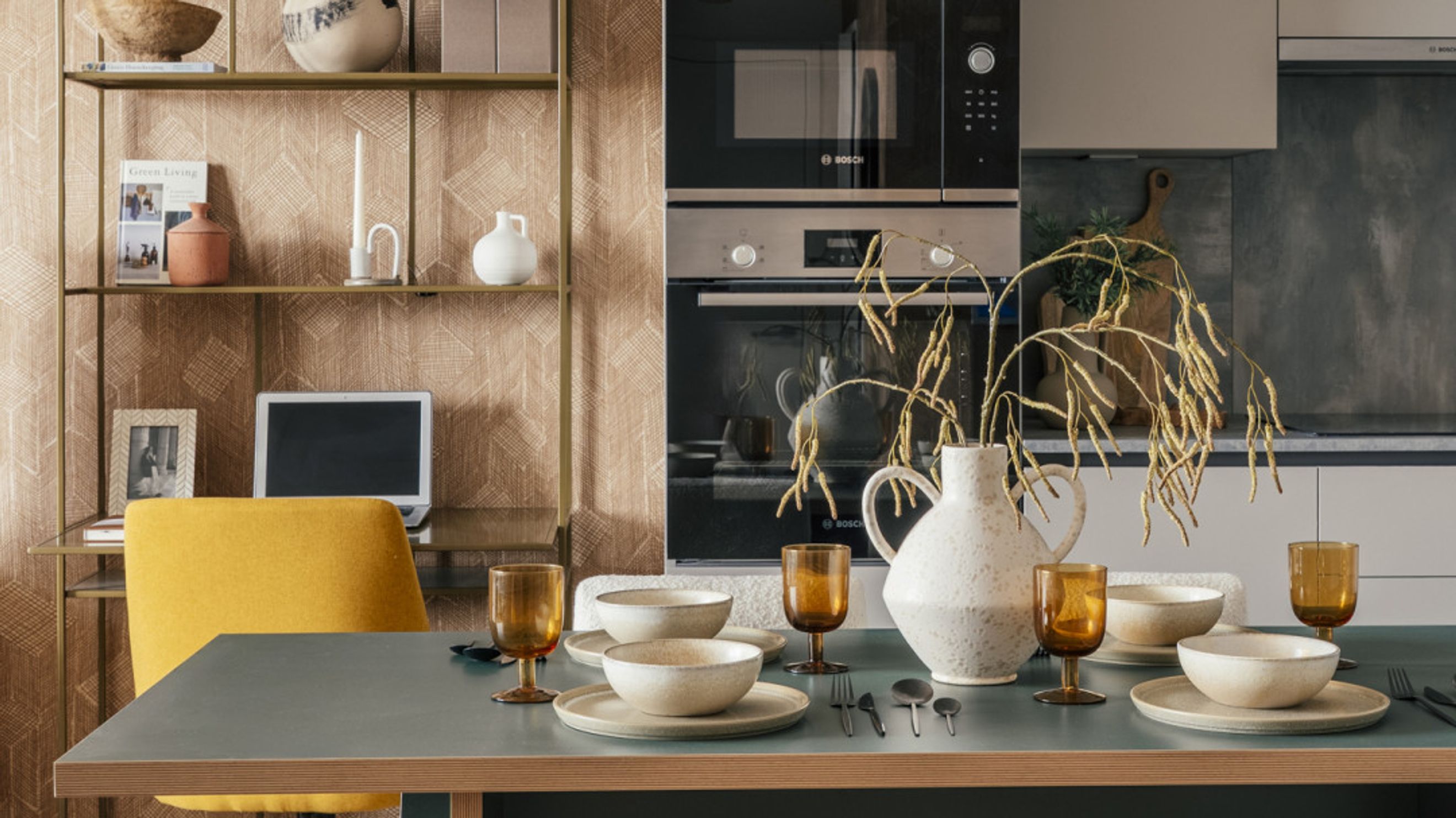 A dining table set for a meal with a yellow chair and a shelf with decor in the background.