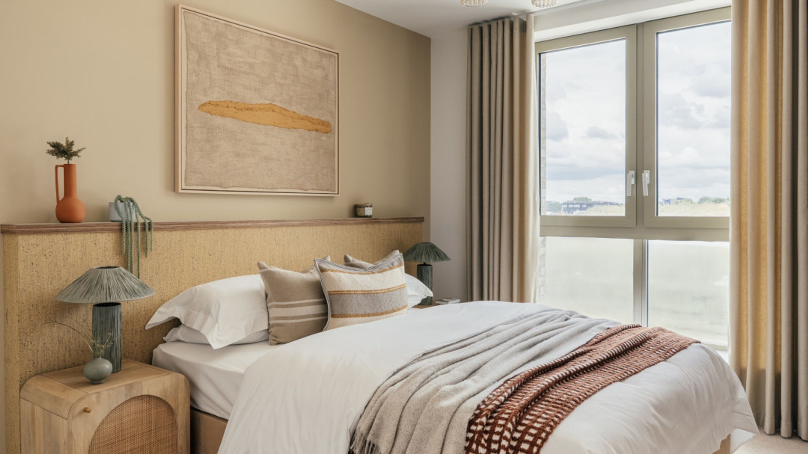 A bedroom with a bed, pillows, a headboard, bedside tables, lamps, and a window with curtains.