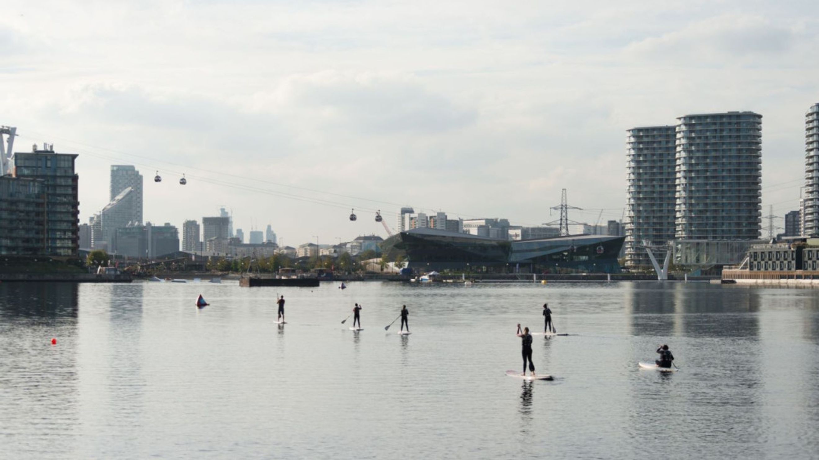 A group of people paddleboarding on a body of water with a city skyline in the background.