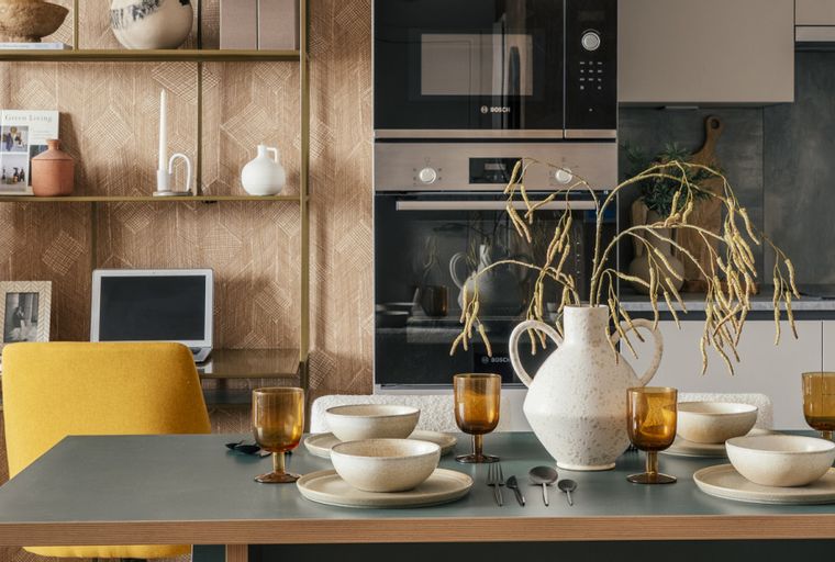 A dining table set for a meal with a yellow chair and a shelf with decor in the background.