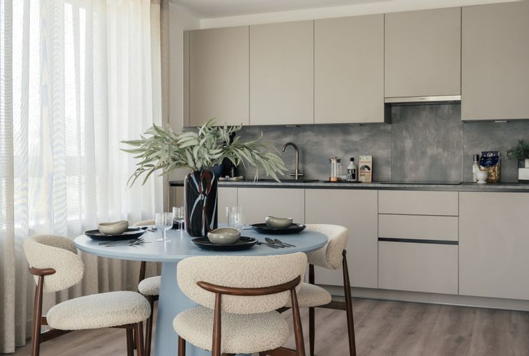 A dining area with a round table and chairs in front of a kitchen with light gray cabinets.