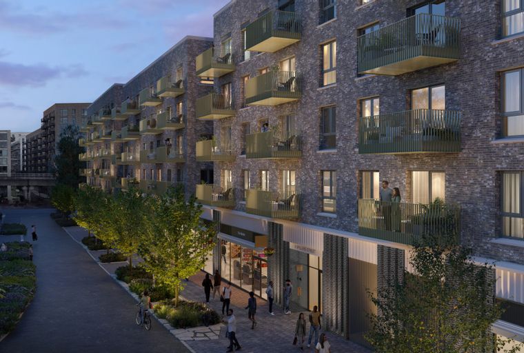 A modern apartment building with balconies and shops on the ground floor, viewed from a street with trees and people.