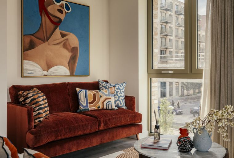 A living room with a rust-colored sofa, decorative pillows, and a large painting.