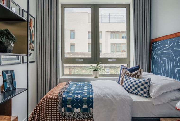 A bedroom with a bed, pillows, a throw blanket, and a window.