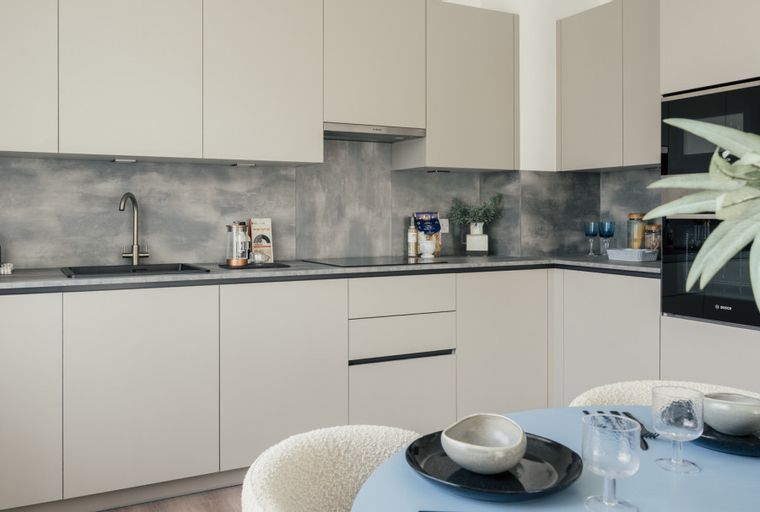A modern kitchen with light-colored cabinets, a grey backsplash, a sink, a hob, and integrated appliances.