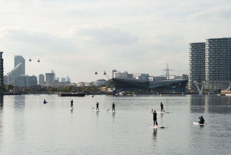 A group of people paddleboarding on a body of water with a city skyline in the background.