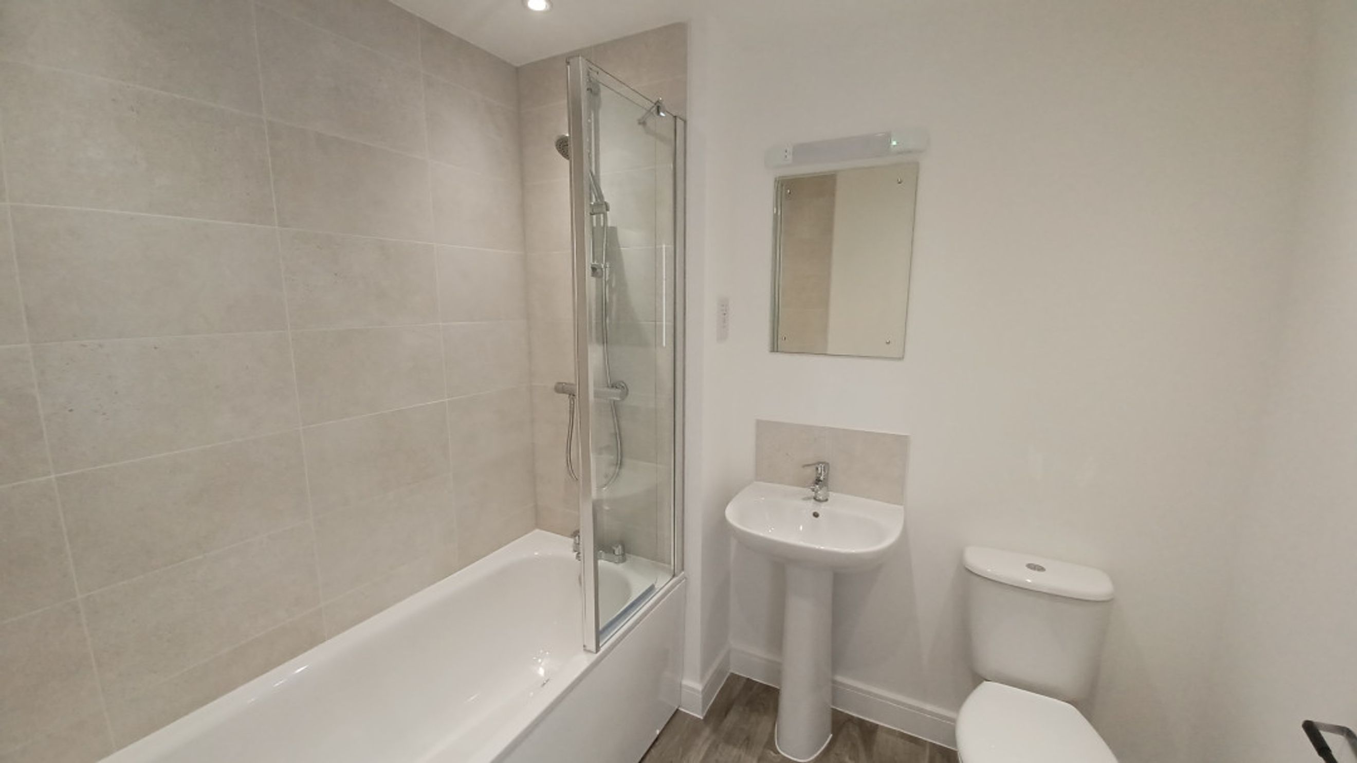 A bathroom with a bathtub, shower screen, sink, mirror, and toilet.