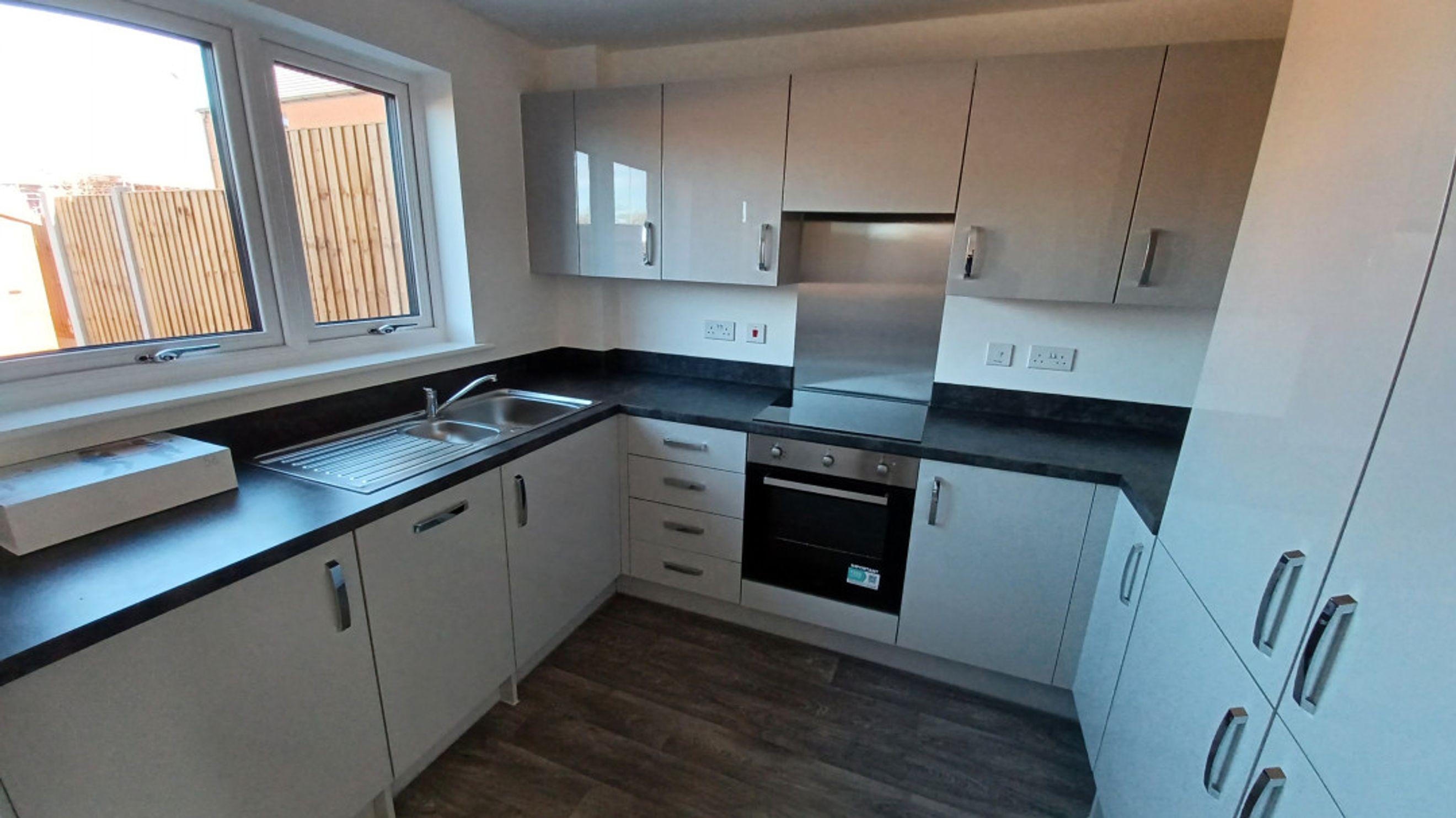 A modern kitchen with white cabinets, a dark countertop, a sink, and an oven.