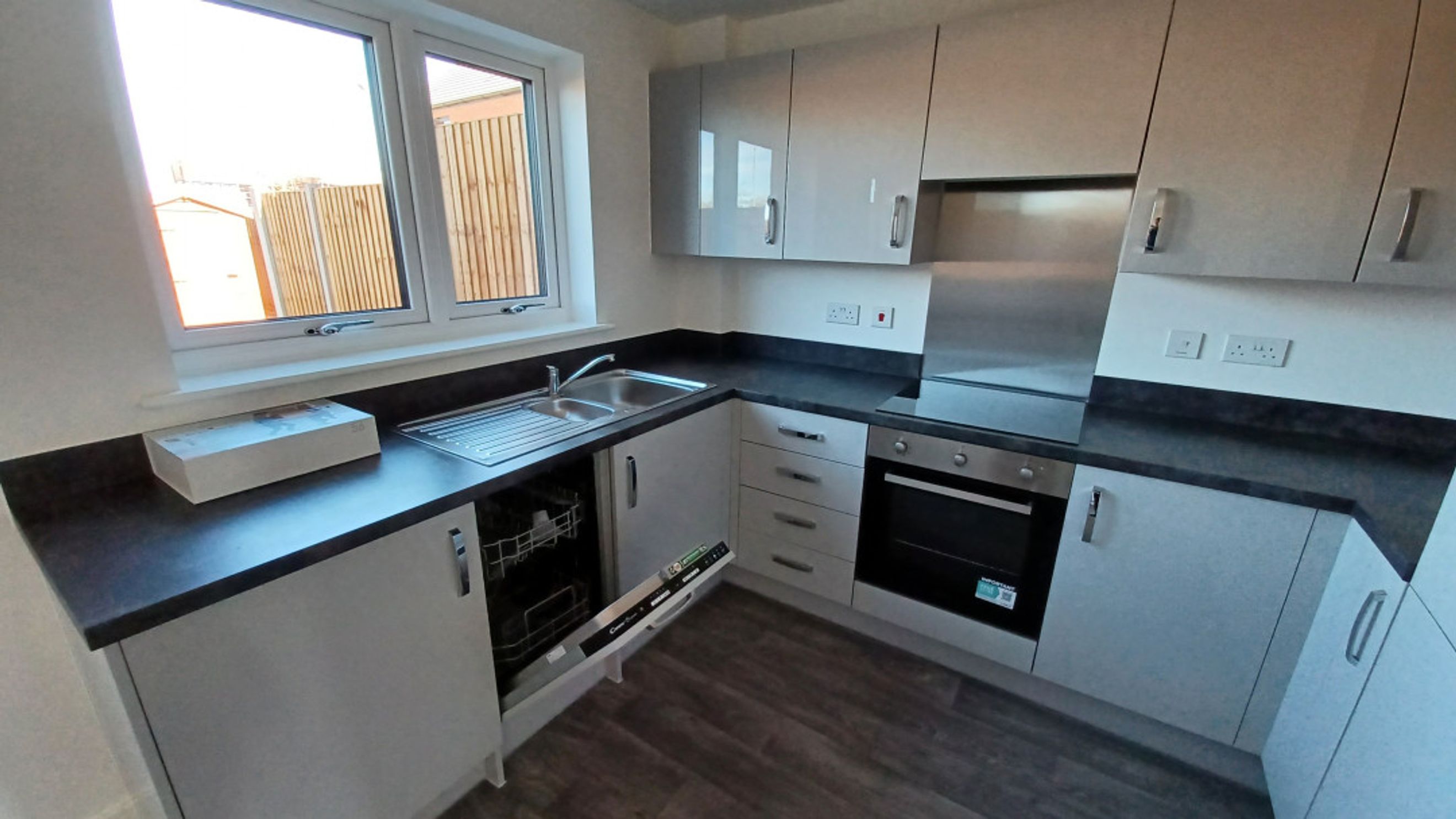 A modern kitchen with grey cabinets, a dark countertop, a sink, a dishwasher, and an oven.