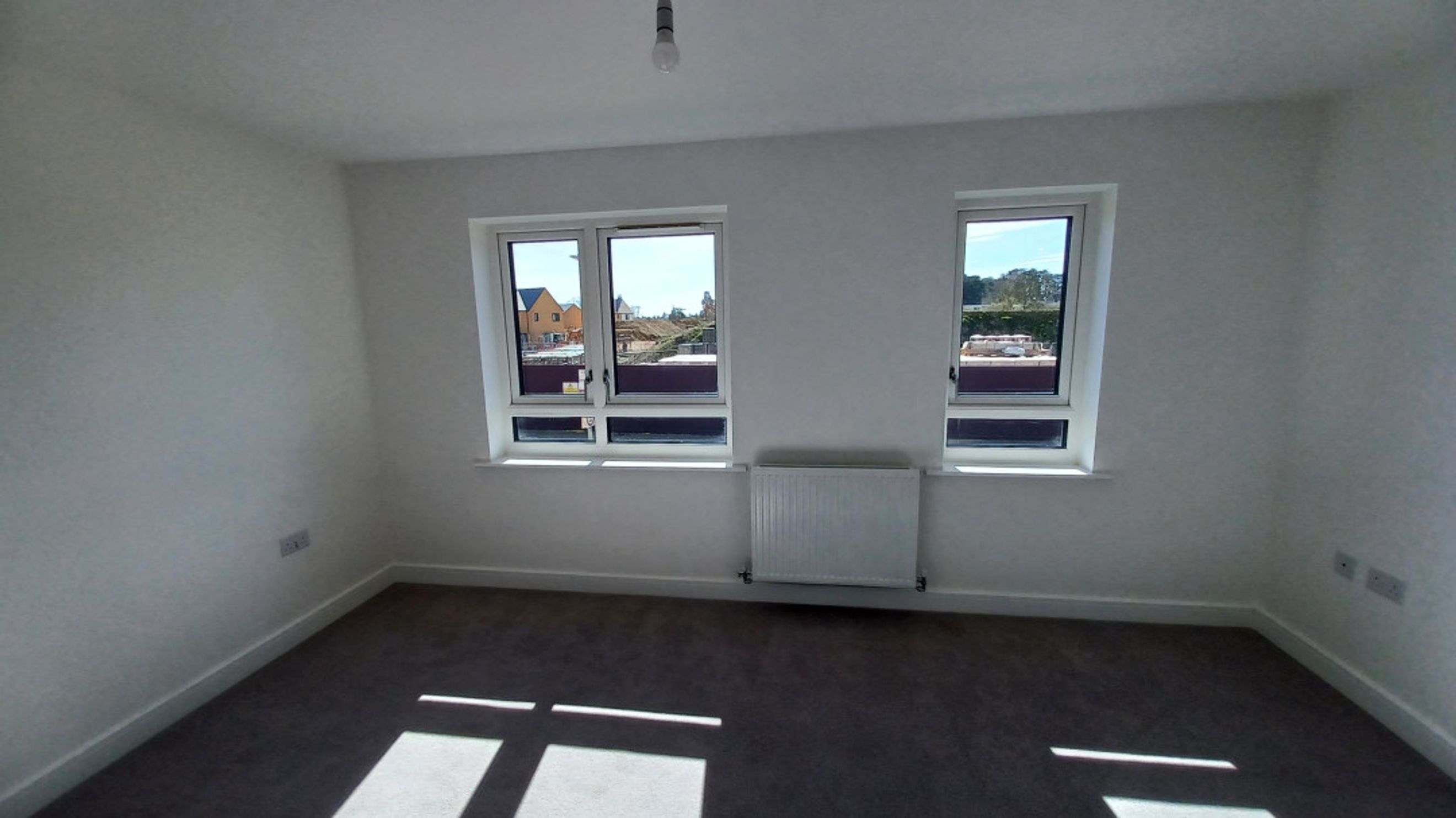 A bedroom with two windows, a radiator, and carpeted floor.