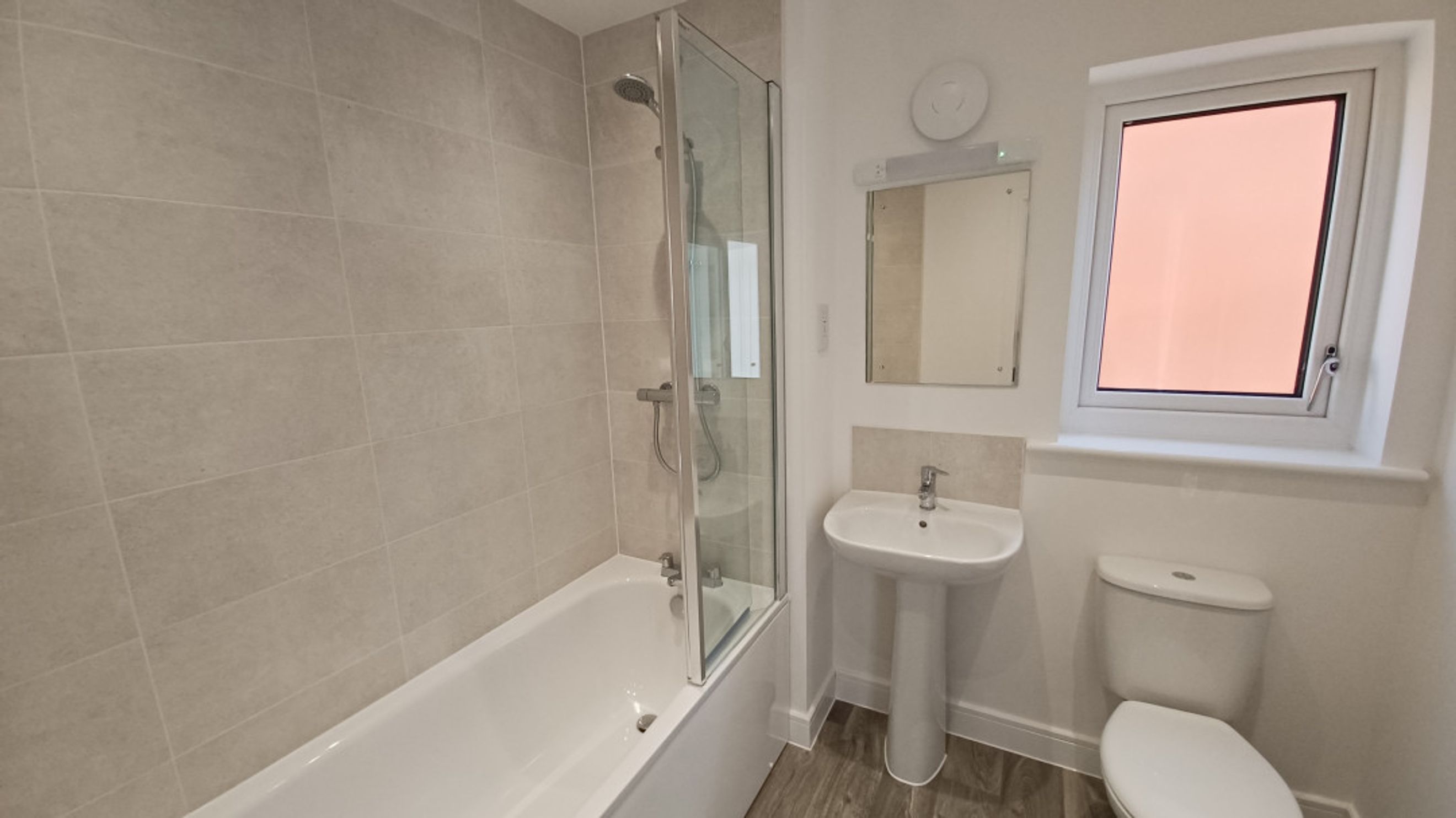 A bathroom with a bathtub, shower screen, sink, toilet, and a window.