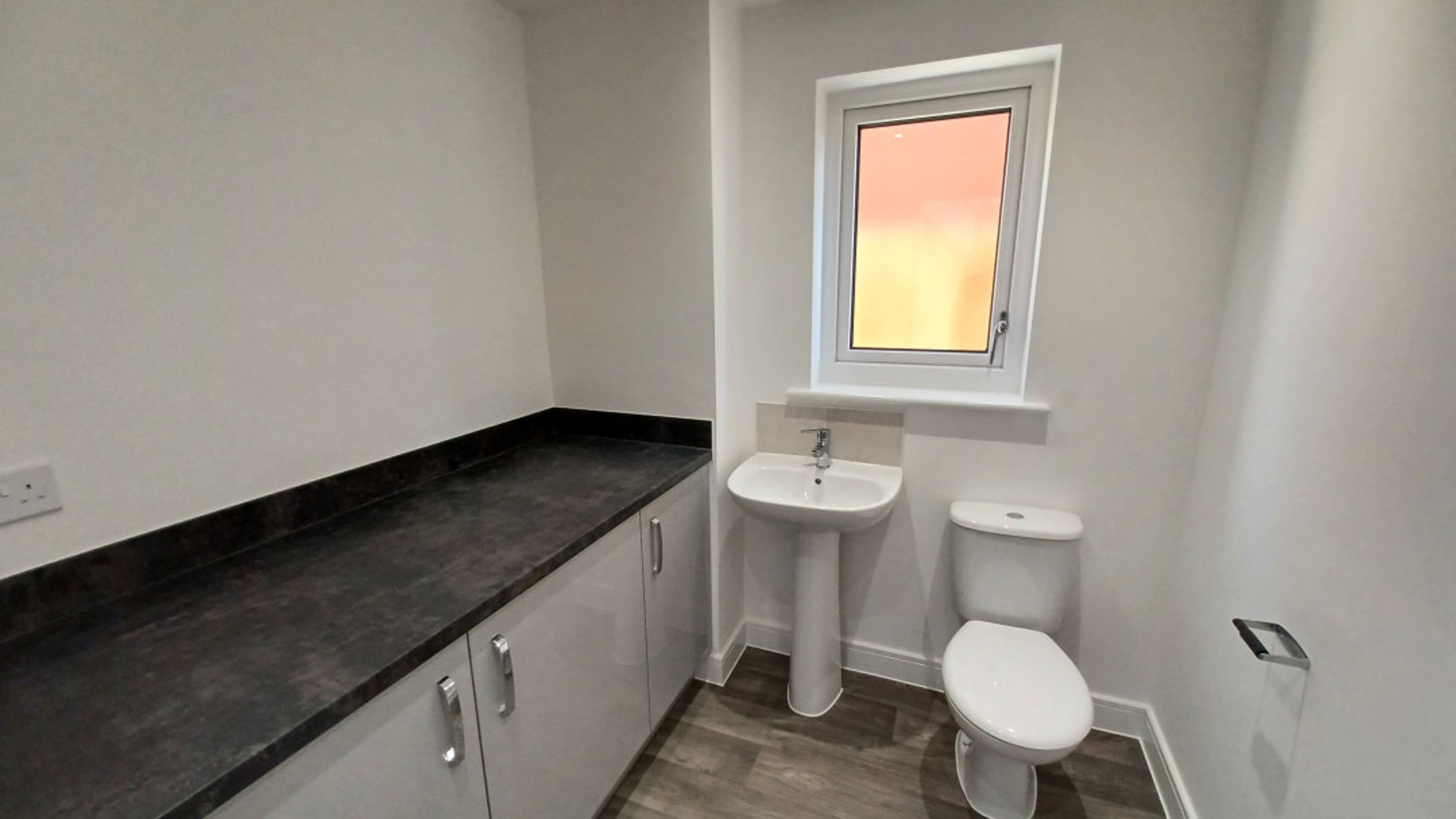 A bathroom with a toilet, a sink, a window, and a vanity with cabinets.