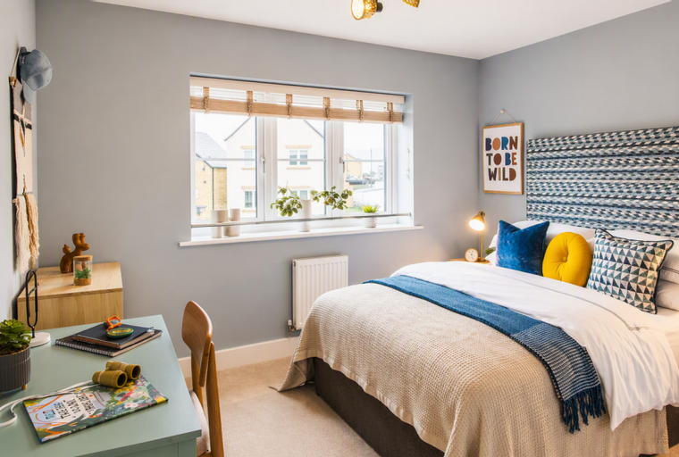 A bedroom with a bed, a desk, and a window.