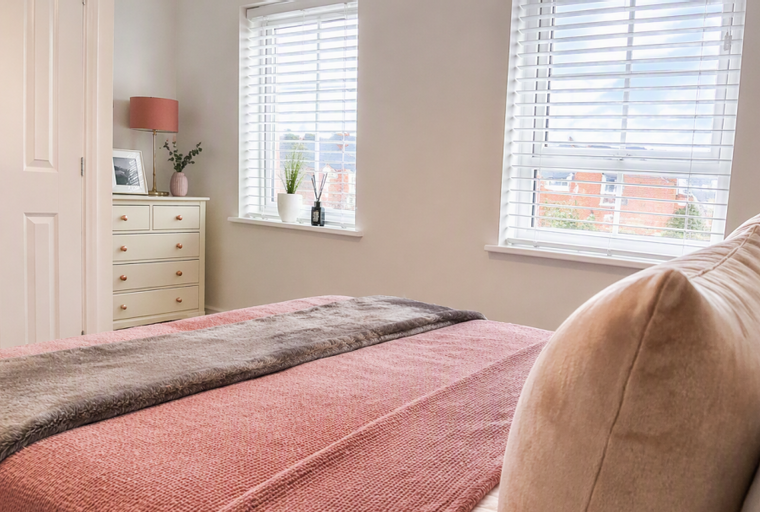 A bedroom with a bed, dresser, lamp, and two windows.