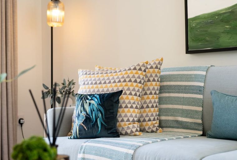A light blue sofa with several decorative pillows and a throw blanket.