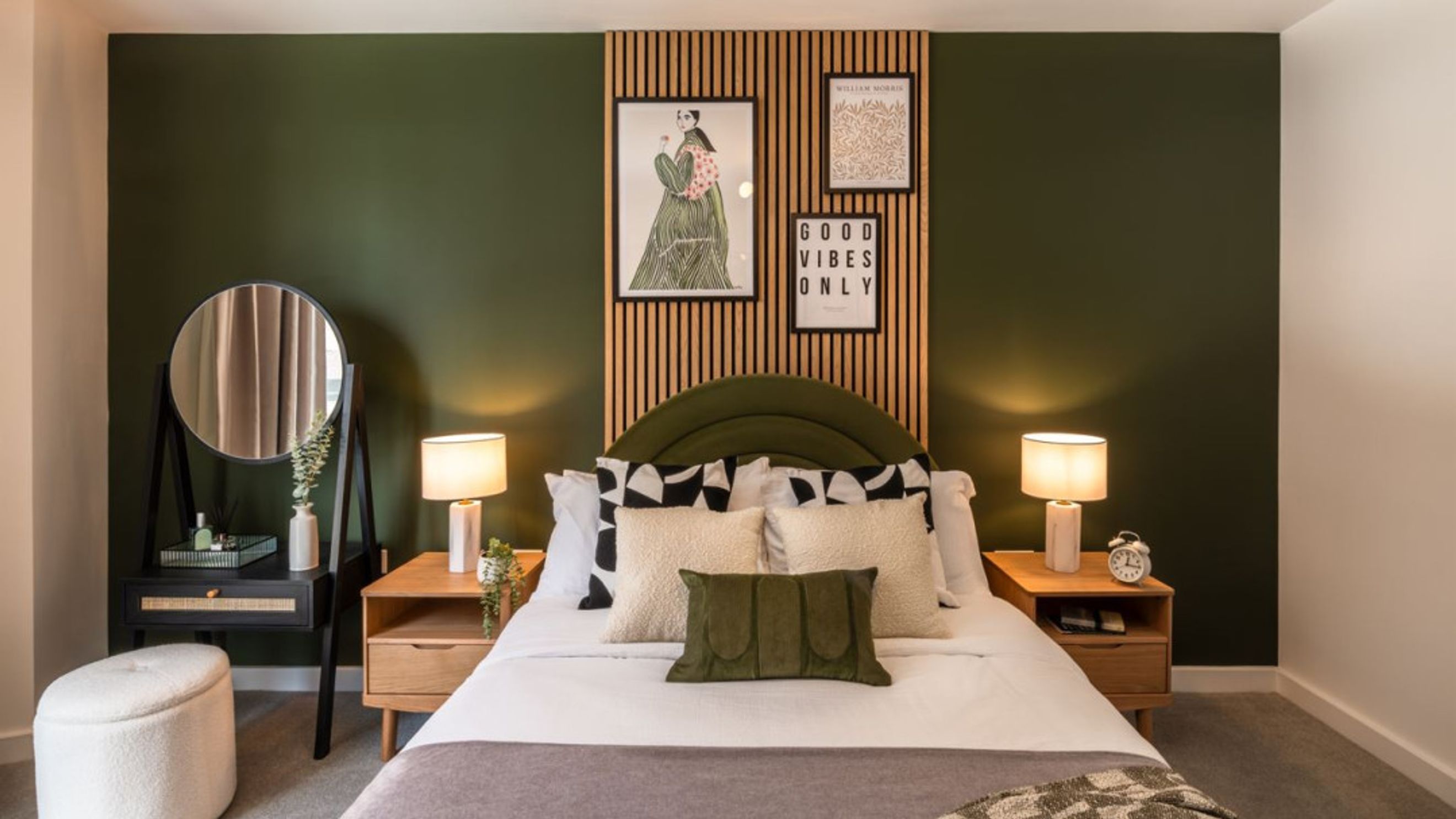 A bedroom with a bed, nightstands, lamps, and artwork on a green wall.