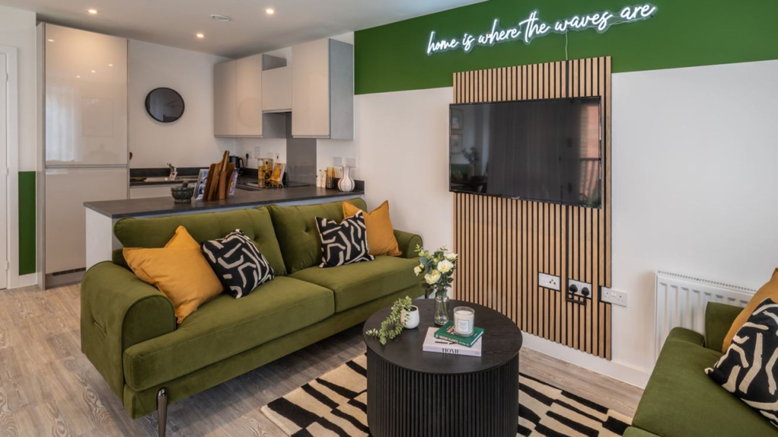 A living room and kitchen area with a green sofa, coffee table, and kitchen cabinets.