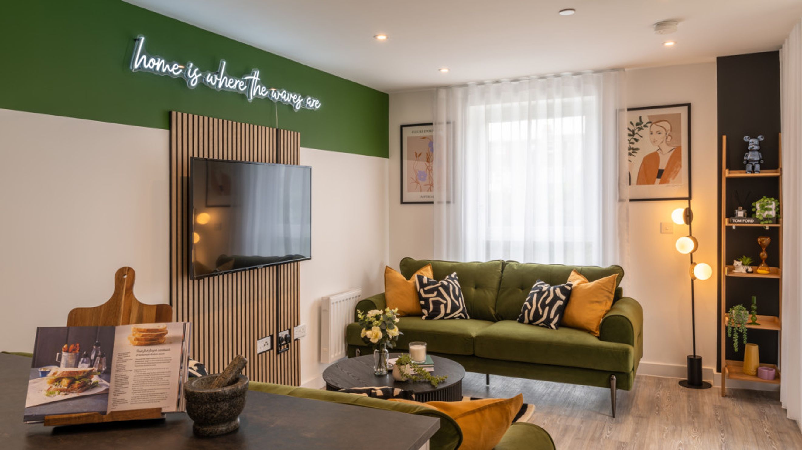 A living room with a green sofa, a coffee table, and a television mounted on a wooden panel.