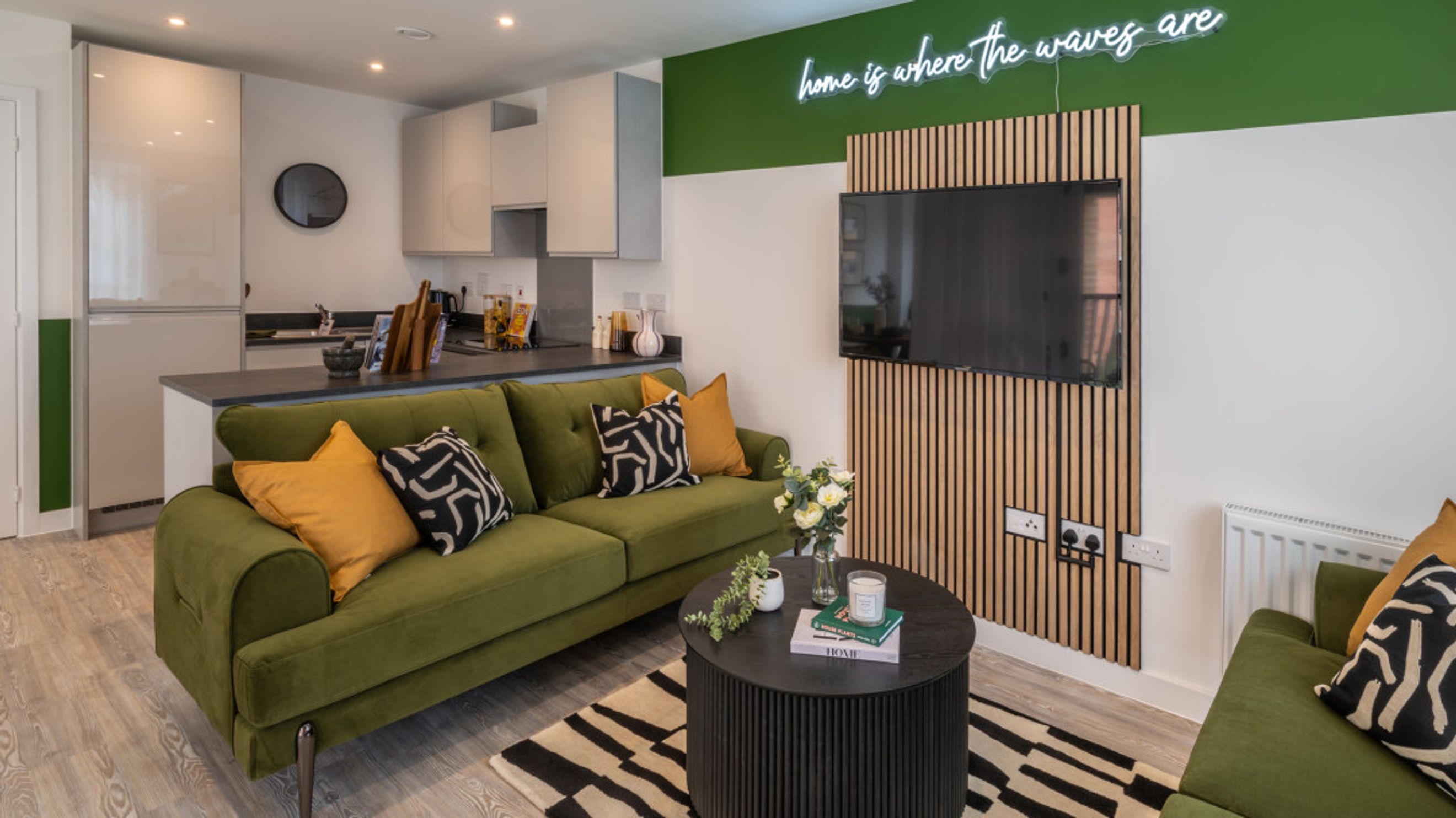 A living room and kitchen area with a green sofa, coffee table, and kitchen counter.
