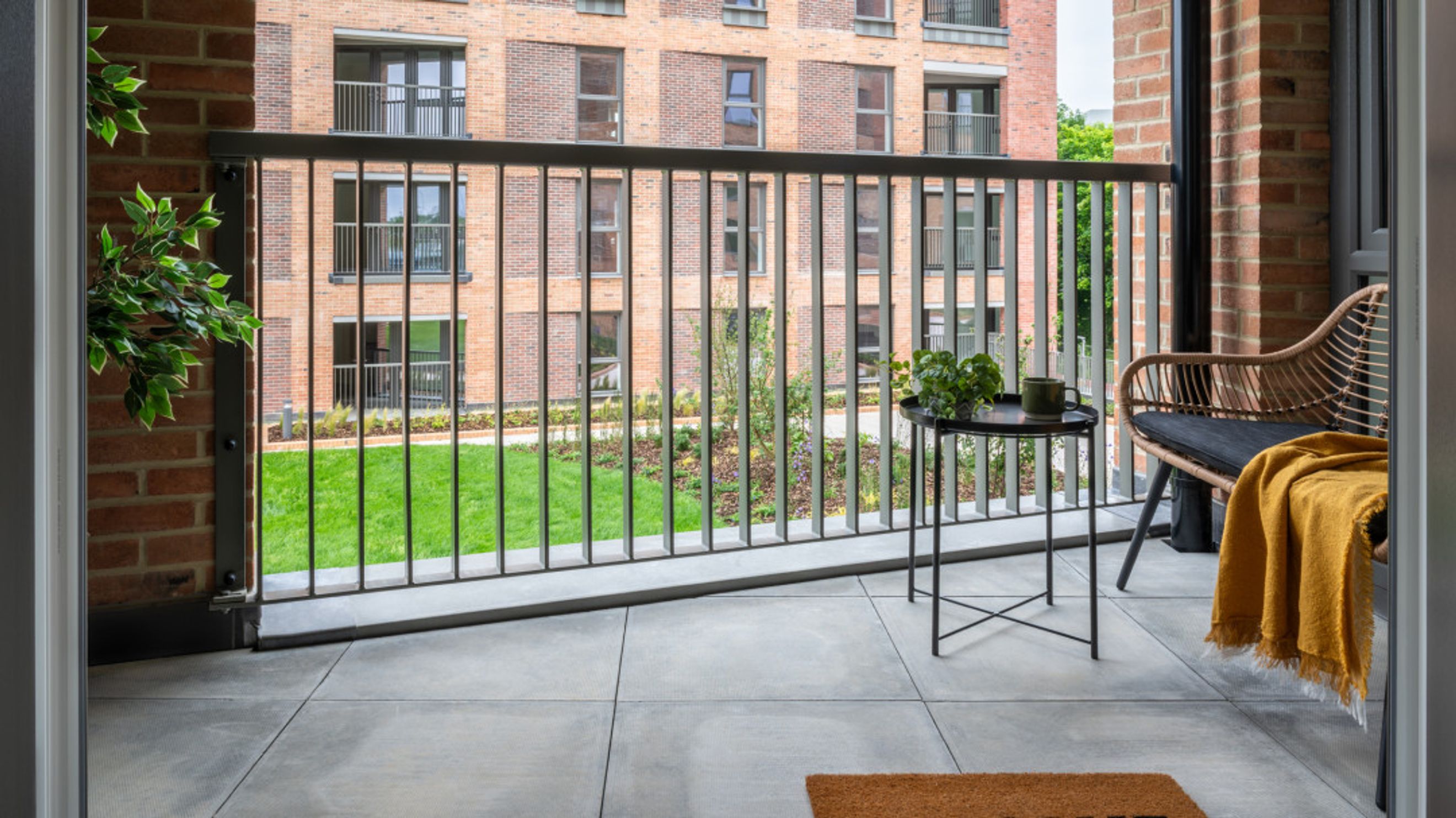 A balcony with a chair, table, and railing overlooking a lawn and building.