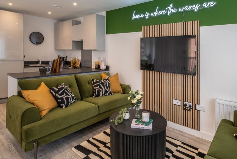 A living room and kitchen area with a green sofa, coffee table, and kitchen cabinets.