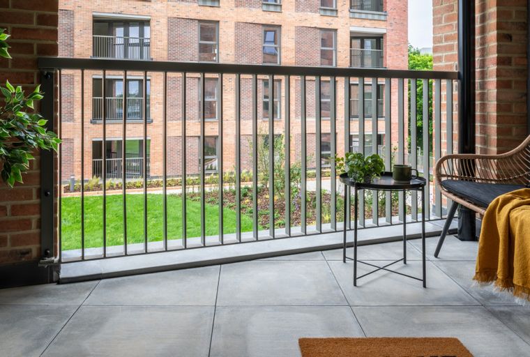 A balcony with a chair, table, and railing overlooking a lawn and building.