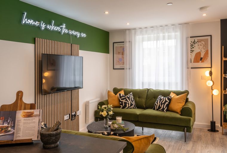 A living room with a green sofa, a coffee table, and a television mounted on a wooden panel.