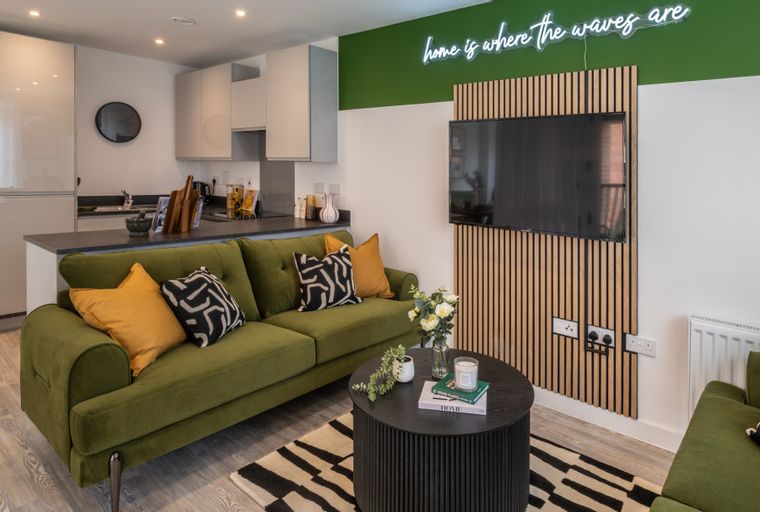 A living room and kitchen area with a green sofa, coffee table, and kitchen counter.