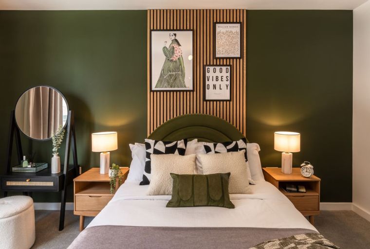 A bedroom with a bed, nightstands, lamps, and artwork on a green wall.