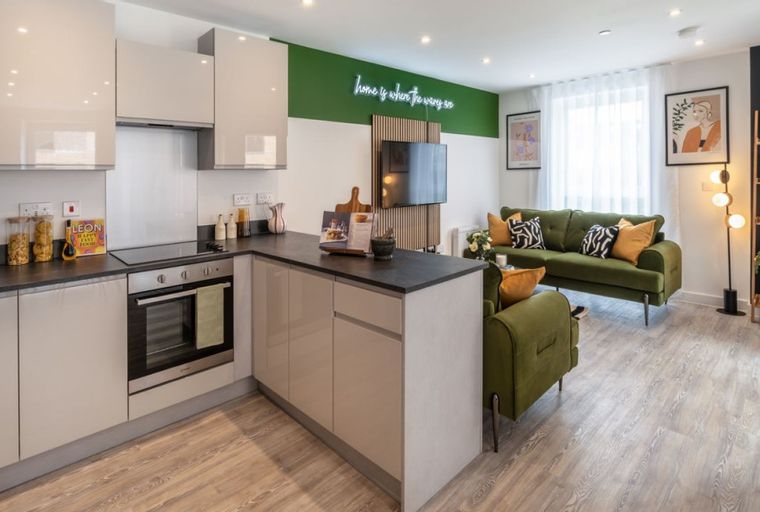 A modern living room and kitchen area with a green sofa, a television, and kitchen cabinets.