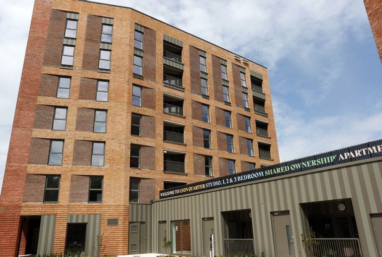 A modern brick apartment building with balconies and a sign that reads 'WELCOME TO LYON QUARTER STUDIO, 1, 2 & 3 ROOM SHARED OWNERSHIP APARTMENTS'.