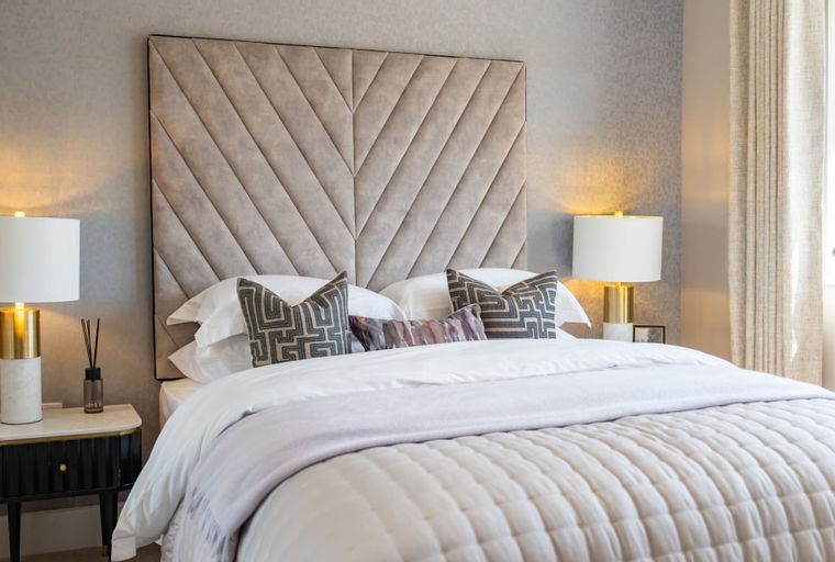 A bedroom with a bed, headboard, pillows, and bedside lamps.