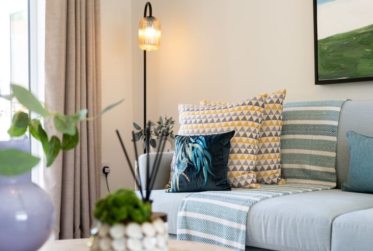 A living room with a light blue sectional sofa, decorative pillows, a throw blanket, and a floor lamp.