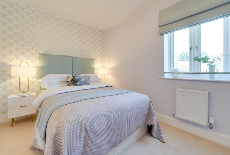 A bedroom with a bed, headboard, bedside tables, lamps, and a window.