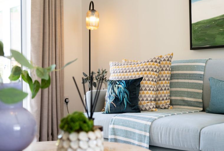 A living room with a sofa, pillows, a blanket, a floor lamp, and a vase.