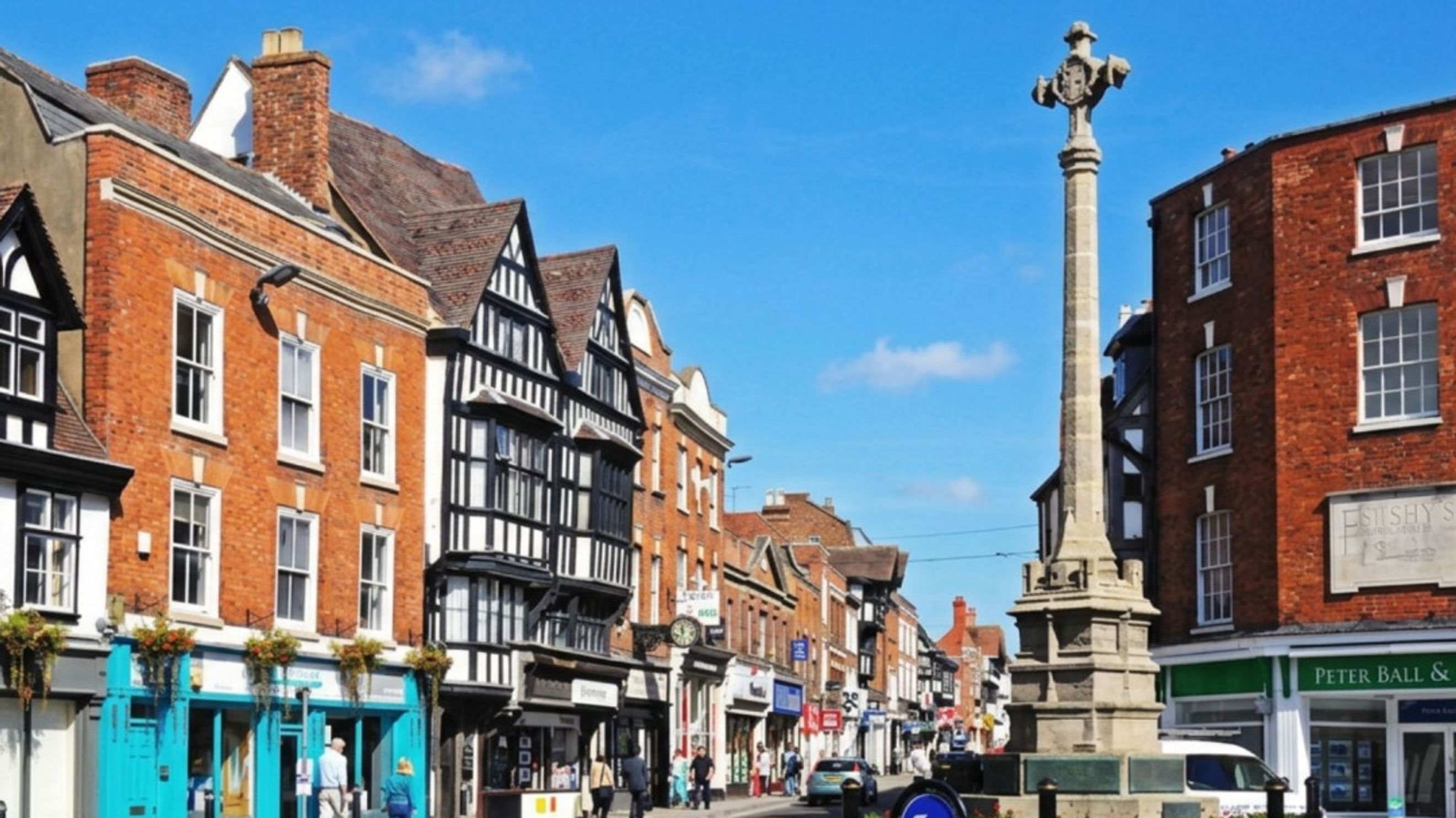A street scene with traditional buildings and a market cross.