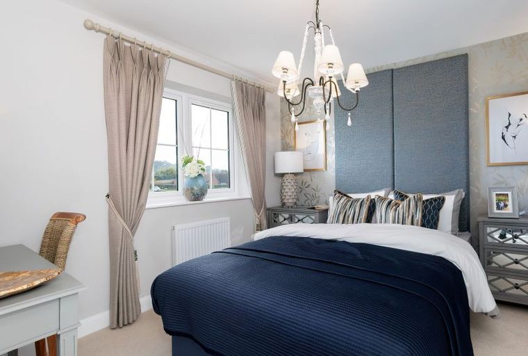 A bedroom with a bed, bedside tables, a chandelier, and a window.