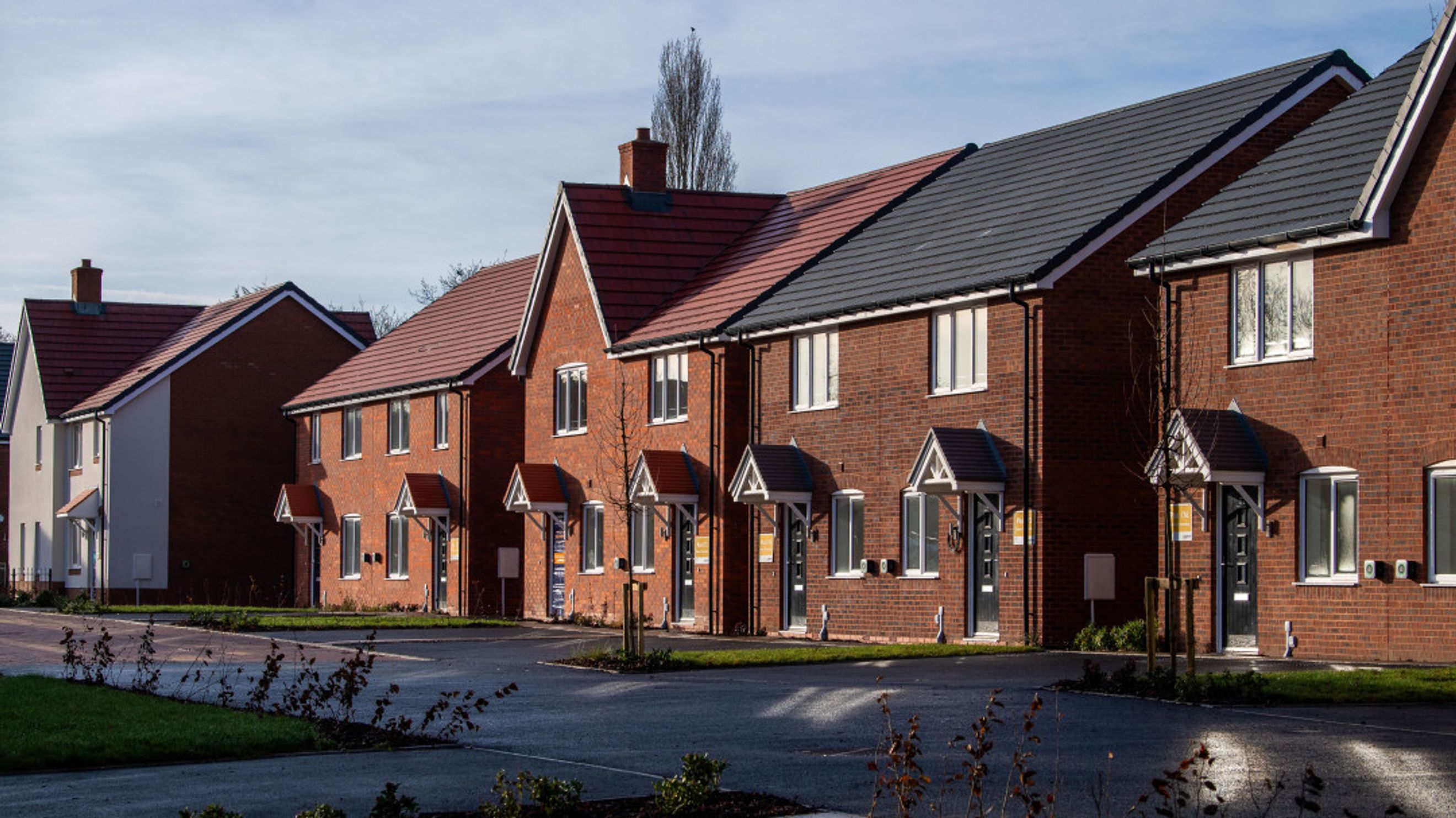 A row of new brick townhouses with pitched roofs and awnings over the doors.