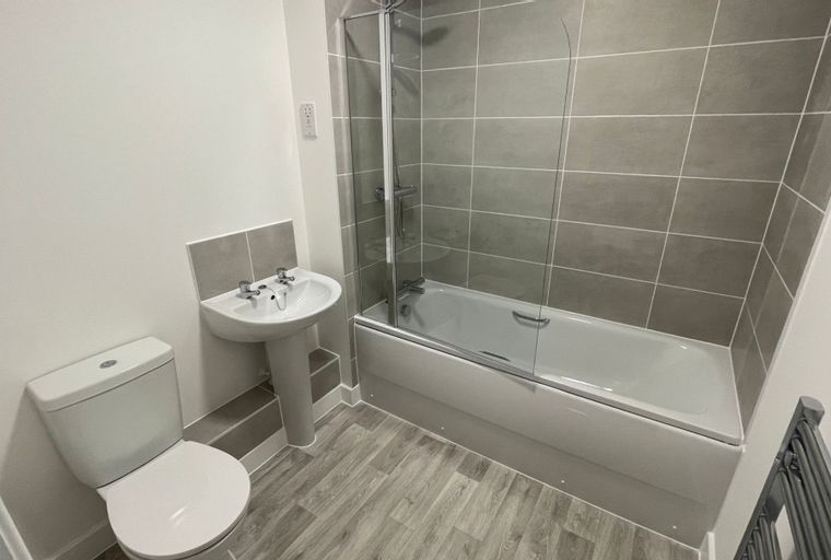 A bathroom with a toilet, sink, and bathtub with a shower screen.
