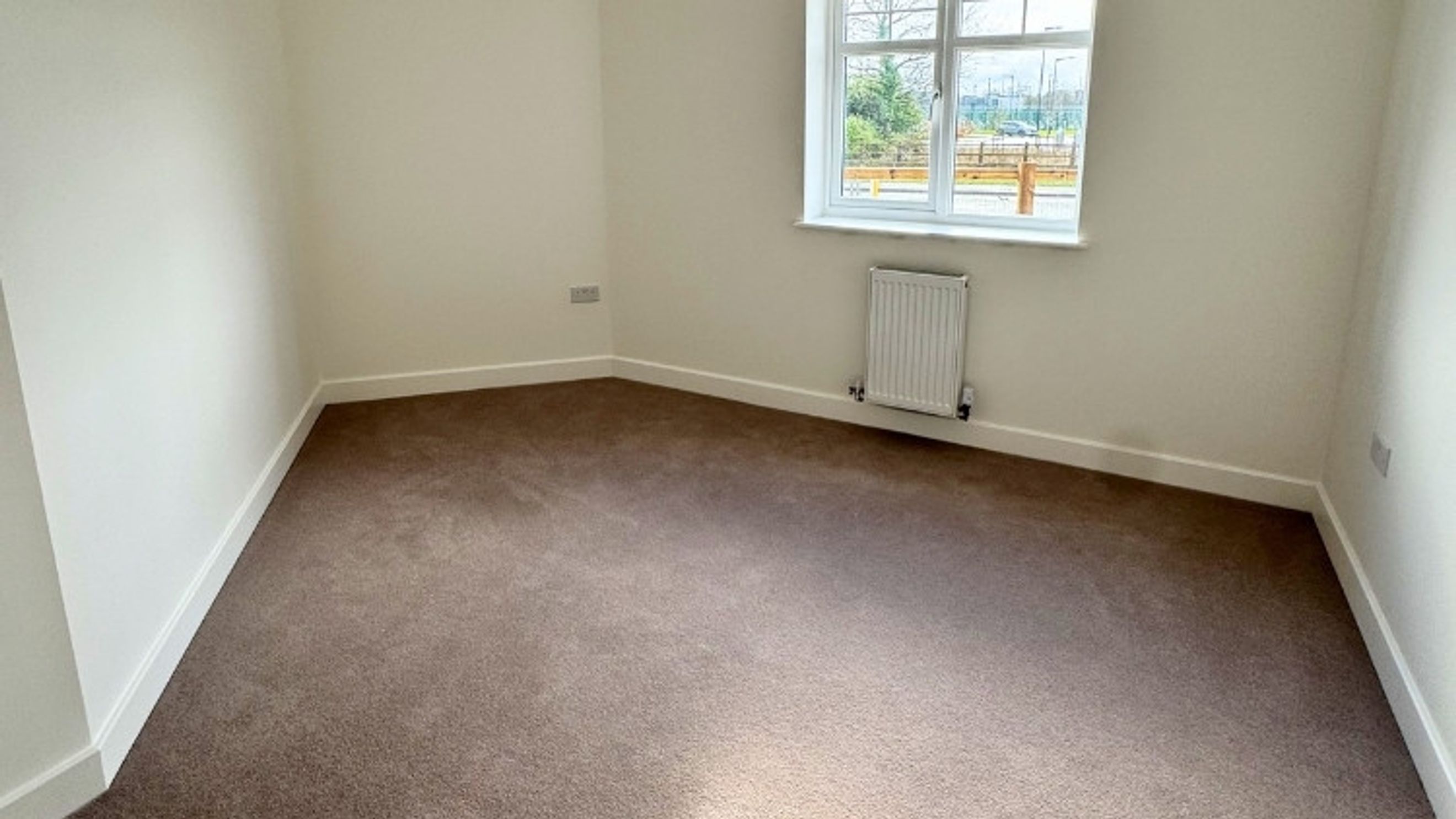 A room with brown carpet, white walls, and a window with a radiator underneath.