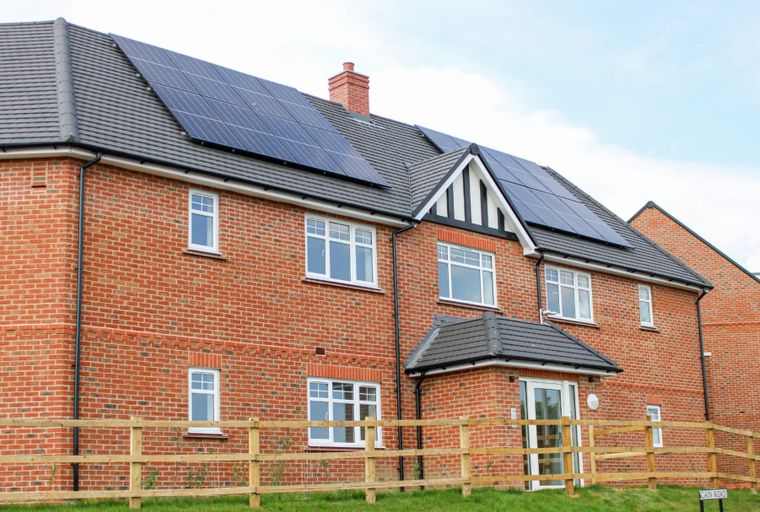 A brick house with solar panels on the roof and a wooden fence in front.