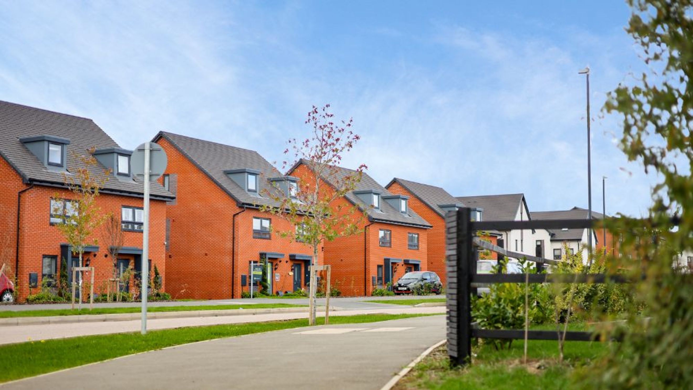 A row of modern brick townhouses with grey roofs and dormer windows under a blue sky.