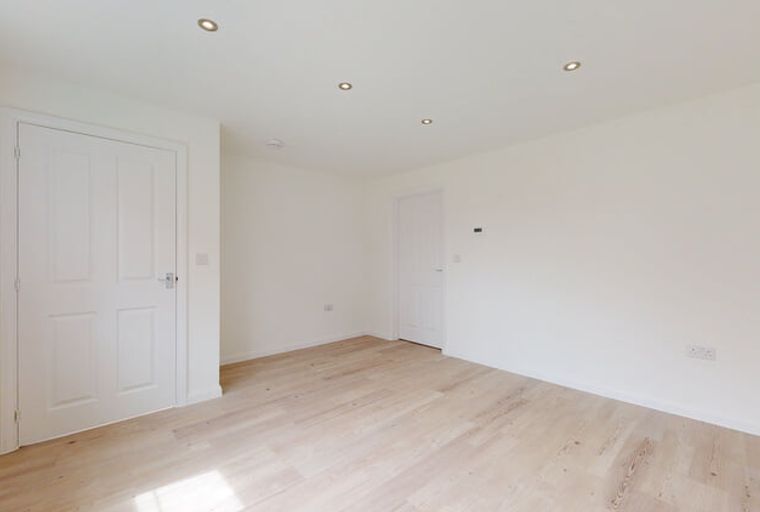 A room with white walls, wooden floors, and two white doors.