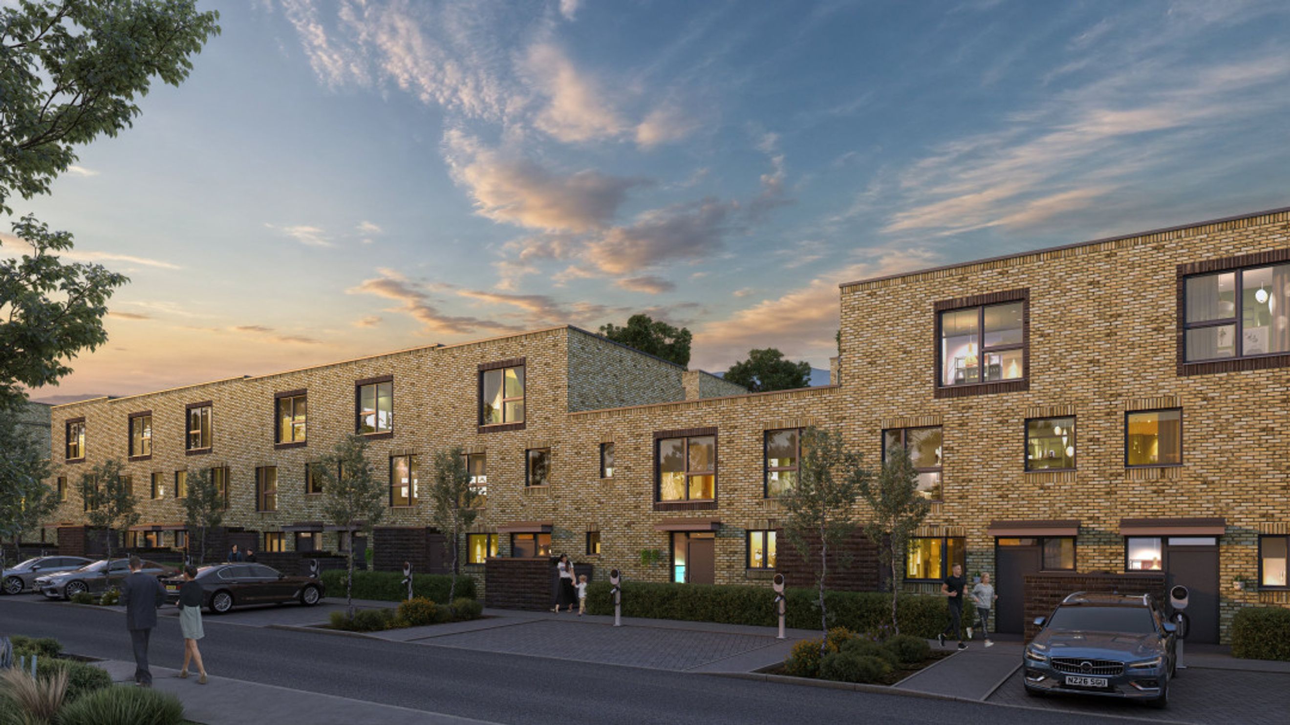 A row of modern brick townhouses with parked cars and people walking on the sidewalk.