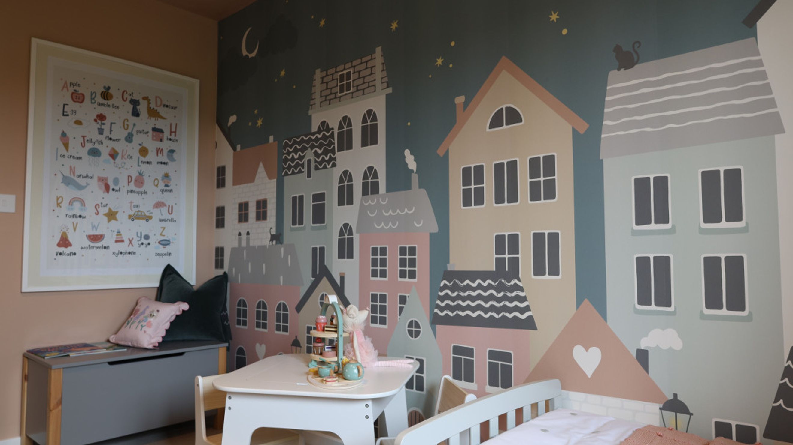 A children's room with a cityscape mural, toy storage, a small table, and a bed.