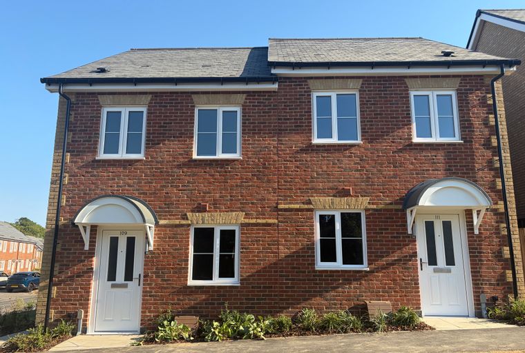 A pair of red brick semi-detached houses with white-framed windows and white front doors under arched canopies.