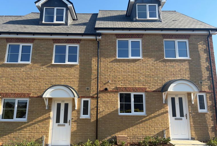 A pair of modern yellow brick townhouses with grey tiled roofs and white-framed windows under a clear blue sky.