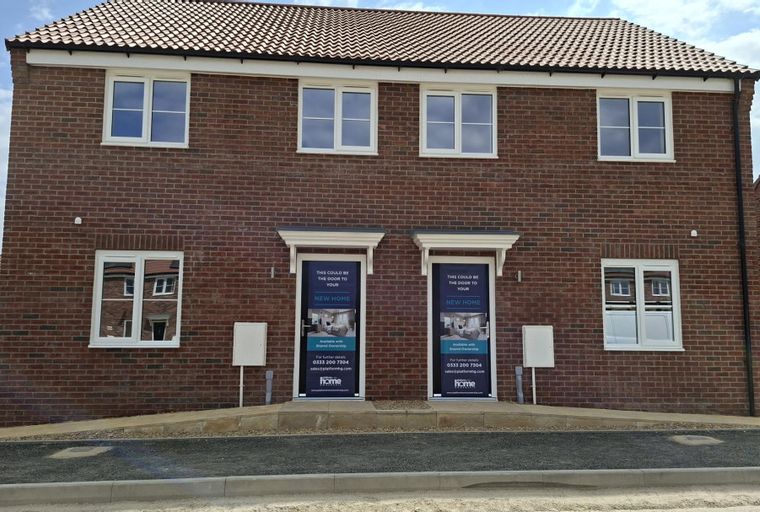 A new brick house with multiple windows and two front doors with banners.