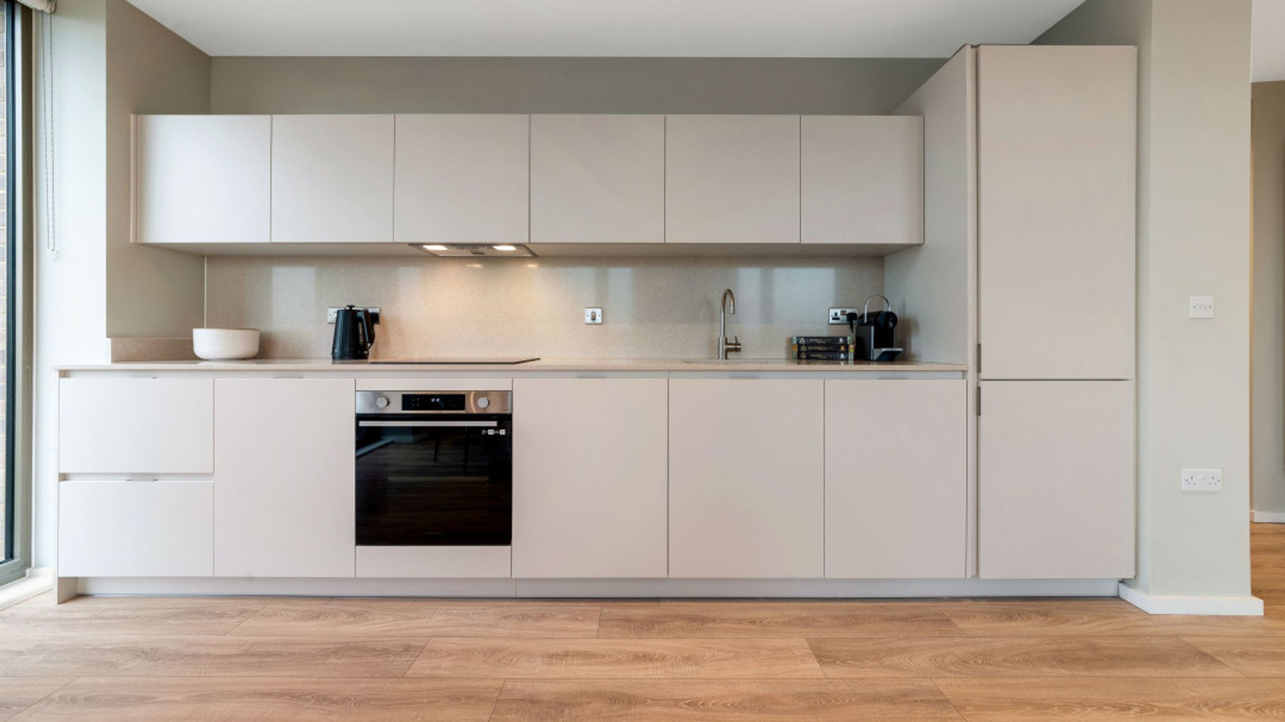 A modern kitchen with light-colored cabinets, an oven, a sink, and a kettle.