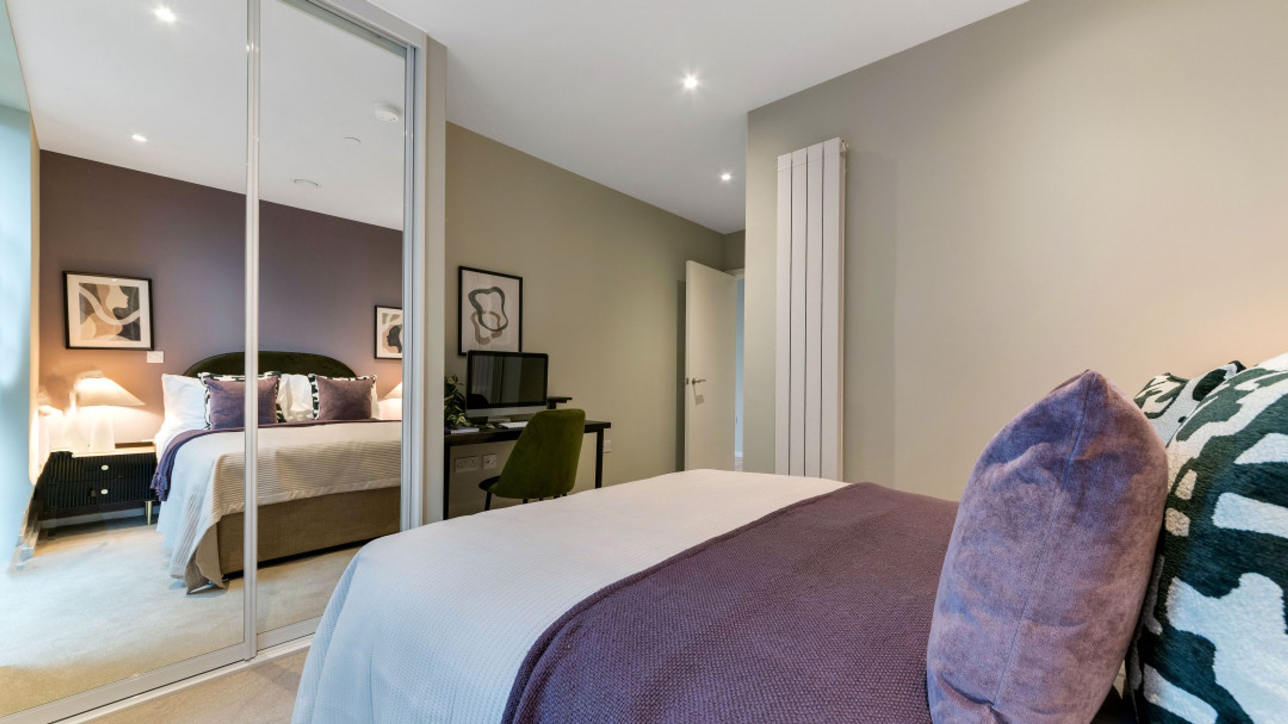 A bedroom with a bed, mirrored wardrobe, and a desk with a computer.